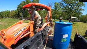 A man filling a tractor with gas from a 50 gallon drum.